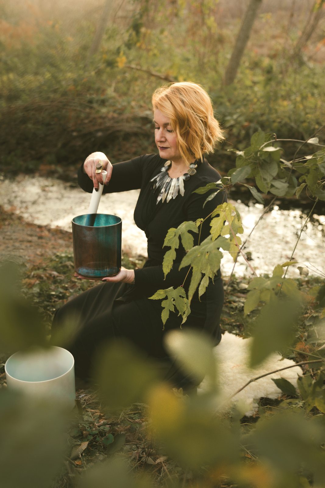 Lara playing a crystal singing bowl by a creek