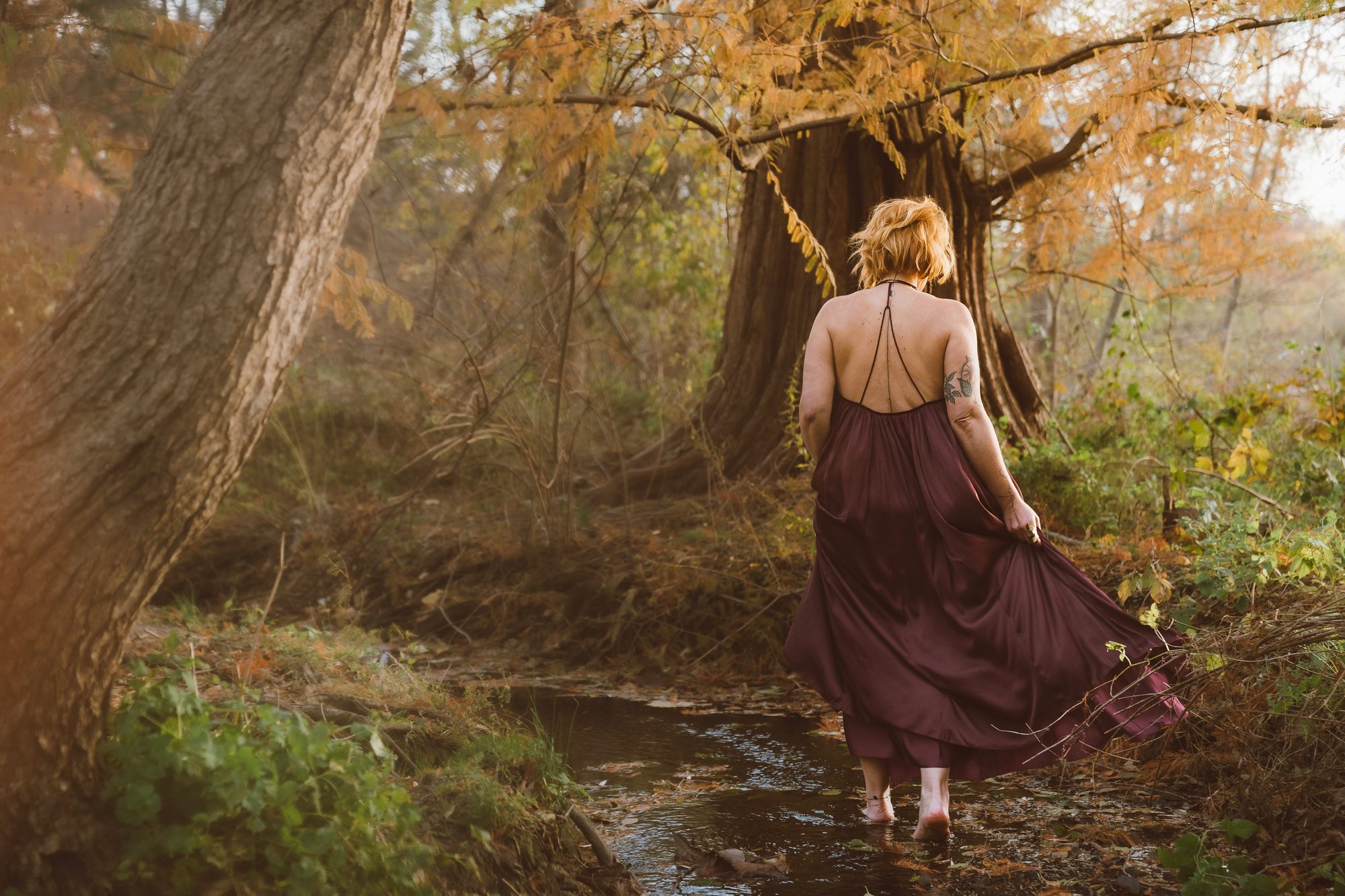 Lara walking through a creek in a flowing dress
